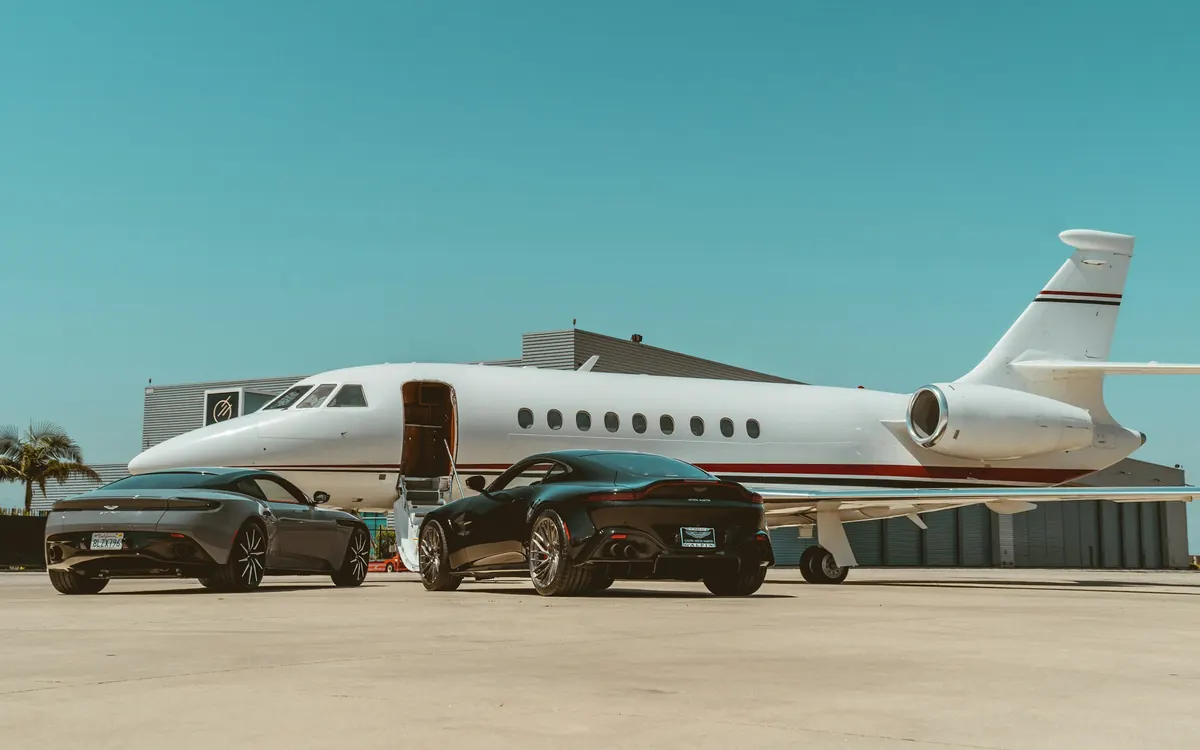 Business jet on a sunny ramp with two cars parked beside it